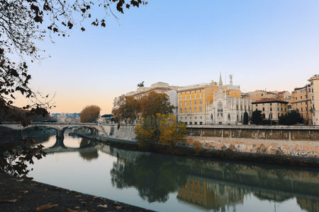 Historic buildings along calm river with stone bridge and autumn trees reflecting in water in Rome cityscape at sunset light, Rome, Italy.のeditorial素材
