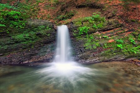Mountain waterfall in the rocky canyon surrounded be green forestの写真素材