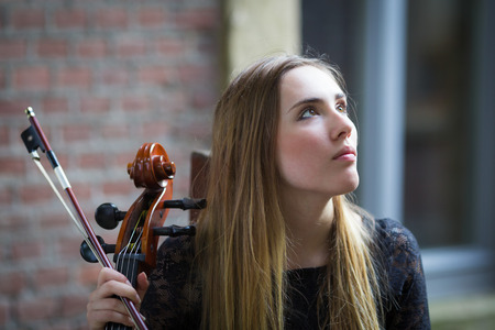 Pretty blonde girl in black dress playing a cello in a rural outdoorの写真素材