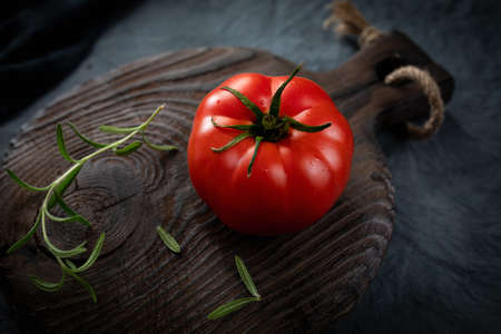 Ripe organic tomato and rosemary sprig on an old chopping board. A crack in a tomato. Selective...