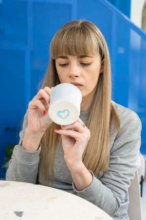 A pretty Caucasian lady paints a mug for her lover. A blue heart is painted on the bottom of the...