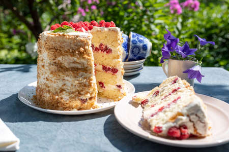 A piece of homemade raspberry sponge cake on a table in the garden on a bright sunny morning. Nearby is a cake without one piece. Summer vacation concept.の写真素材