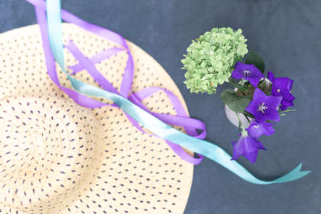 Women's straw hat, ribbons and a small bouquet of green hydrangeas and bells on a dark blue background. Summer vacation concept. Image for blog or advertisingの写真素材