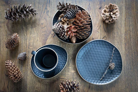 Dark blue set of dishes: tea cup, saucer, plate, a bowl with fir cones, variety of cones on wooden...