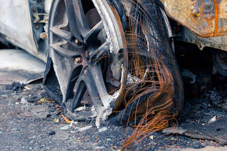 Wheel of burned car. Burnt flat tire on the car is on the gray asphalt road to illustrate an article about a fire, banditry, an insured event, loss compensation.の写真素材