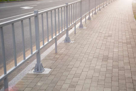 A metal fence between the roadway and the sidewalk. An empty pedestrian path with a fence. Multi-lane road with a pedestrian path next to it separated by a railing.の写真素材