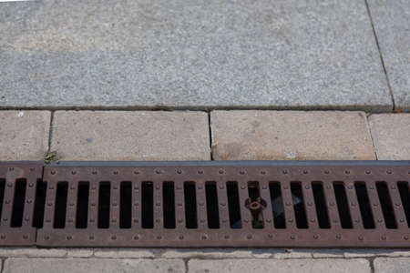 A rusty storm drain grate on the side of the road. Urban infrastructure, road protection from floods, heavy rainsの写真素材