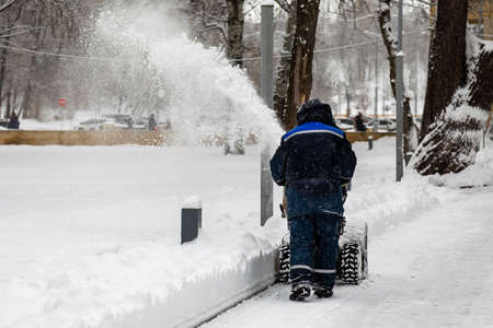 Man clearing or removing snow with a snowblower on a snowy road in the parkの写真素材