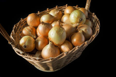 Ripe golden onion in a wicker basket on a black background. Autumn gifts, harvest season.の写真素材