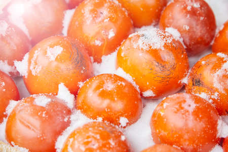 Brightly persimmon fruit in a box covered with snow. The concept of the beginning of winter, white Christmas.の写真素材