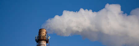Factory chimney blowing smoke from pipe in blue sky background during winter time. Air pollution and...