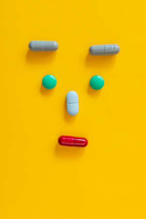 minimalistic image of a human face from pills and pills on yellow background. Verticalの写真素材