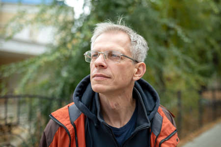 Portrait of a smiling Mature gray-haired man in casual autumn clothes on a city street. Looking away from the cameraの写真素材