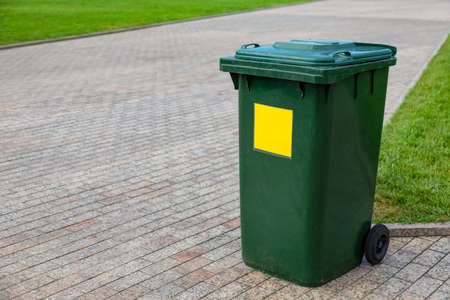 Plastic green garbage can for collecting garbage in the park. Mobile trash can with wheels. A yellow sign marks plastic waste. Close-upの写真素材