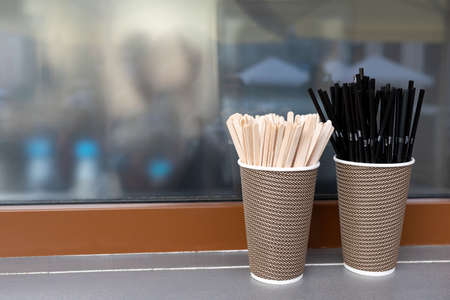 Black cocktail tubes with corrugation, wooden stirring sticks in paper cups in front of a coffee...