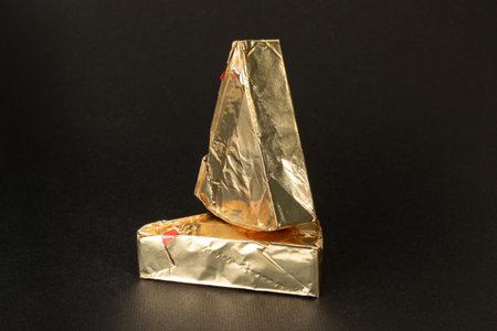 Triangular cream cheeses wrapped in foil on a black background. Portioned triangular cheeses.