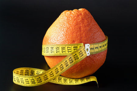 Fresh grapefruit wrapped with measuring tape on a black background. The concept of healthy nutrition, weight loss, dieteticsの写真素材