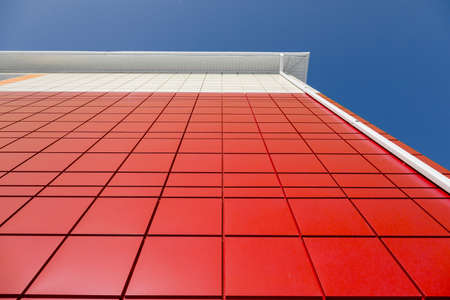 a fragment of a red aluminum ventilated facade with aa drainpipe on a blue sky background