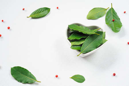 Fresh bay leaf. Laurel in a white heart-shaped plate and pink pepper Schinus terebinthifolius on a...