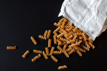 Whole grain eggless rye fusilli pasta on a black background spilled out of white paper bag. Top viewの写真素材