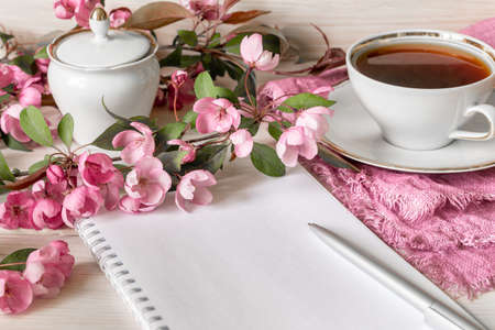 A branch of a blooming apple tree, an empty notebook for notes and a pen and a cup of tea on a...
