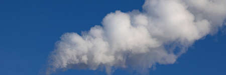 white smoke like a cloud against a blue sky in winter. White steam or smoke is blown in the wind...