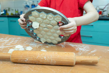 Shaking out ready raviolis, meat dumpling or pelmeni, from mold. Teaching children to cook homemade food, joint work. Selective focus.の写真素材