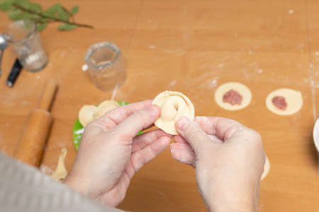 Woman's hands sculpting ravioli, meat dumpling or pelmeni from rolled dough discs and pieces of minced meat. Cooking delicious homemade foodの写真素材