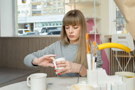 lady cleans a white pitcher with sandpaper before applying the pattern to the clay product