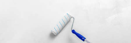 A paint roller with white paint on the background of a textured white wall.