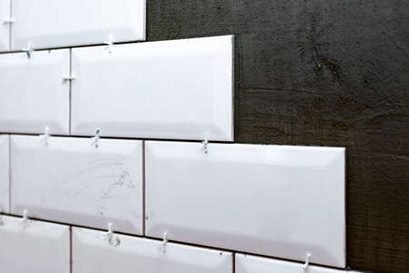 A real photo of laying tiles on the wall. Stained white ceramic tile and a layer of tile glue on the wall. Plastic tile spacer or tile cross between tiles. copy spaceの写真素材