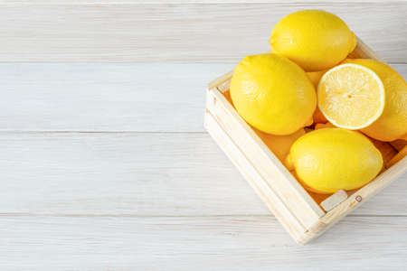 Fresh lemons in a wooden box on a white wooden background. Ripe and tasty citrus fruits. Copy space for textの写真素材
