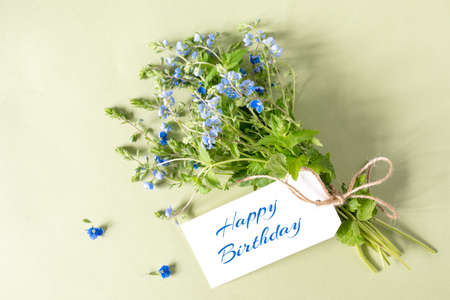 Happy Birthday greeting card and a cute bouquet of blue wildflowers Veronica on a light yellow backgroundの写真素材