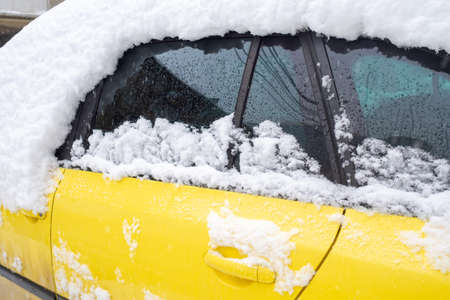 A fragment of a yellow car covered with snow. Bad weather, snow storm, winter.の写真素材