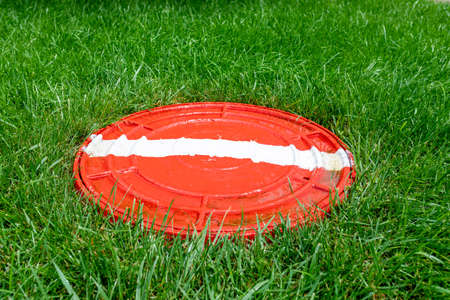 Red hatch with a white stripe on a green lawn. Sewer cover or fire hydrant hatchの写真素材