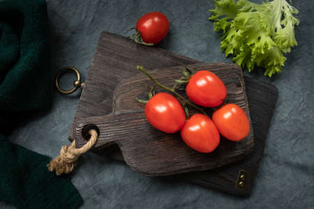 a branch with red ripe cherry tomatoes on a decorative kitchen board and a leafes of fresh frieze lettuce. Farm organic products. Farm organic products, diet, healthy food conceptの写真素材