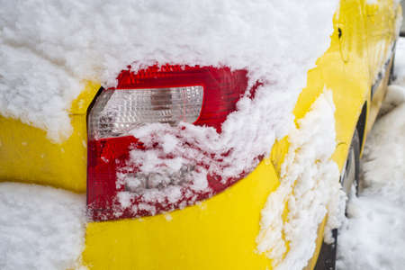 A car covered with snow after a snowfall. The taillight of an unrecognizable yellow car among a snowdriftの写真素材
