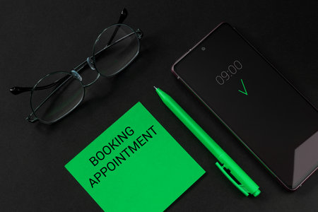 Booking appointment. Appointment reminder on a green tear-off sheet from the block, pen, glasses and smartphone on a black backgroundの写真素材