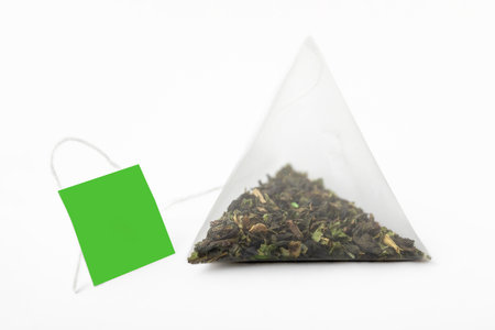 Tea Time. Pyramidal green tea bag with a green label on a white background. Tea bag pyramid shape. Close-upの写真素材