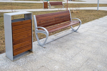 Wooden bench with backrest and trash can on sidewalk in the cityの写真素材