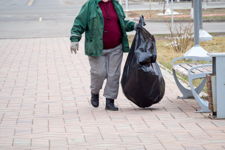 A person at work collecting trash in a park, symbolizing community cleanliness and environmental responsibility. Waste management, public service, and urban maintenanceの写真素材