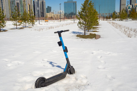 Blue electric scooter in snow in urban park for illustrating winter urban scenes, transportation, and weather conditions. Inclement weather, unexpected snowfall.の写真素材