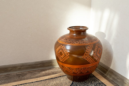 A decorative ceramic vase with intricate patterns sits on the floor, casting a soft shadow, adding warmth and cultural charm to the space.の写真素材