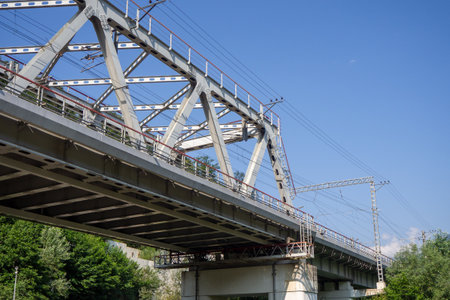 Steel railway bridge in alpine valley. Mountain transport infrastructure. Train bridge over green slopes and blue sky.の写真素材