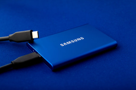 Samsung portable SSD T7 with two connected USB Type C cables on a vibrant blue surface. Compact and efficient external storage for modern devices. Astana, Kazakhstan - July 16, 2025のeditorial素材