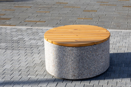 Round bench with concrete base and wooden seat on a paved sidewalk. Resting place in an urban...