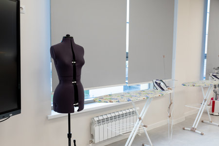 Tailor mannequin and sewing equipment in bright workspace. Tailor dummy, ironing boards in a modern sewing workshop. Photoの写真素材