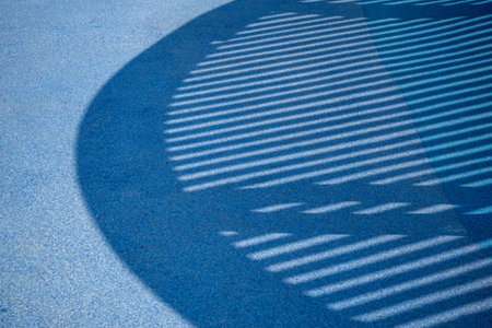 Blue rubber sports coating with shadows. Urban recreation area. Modern playground or workout zone with safe surface.の写真素材