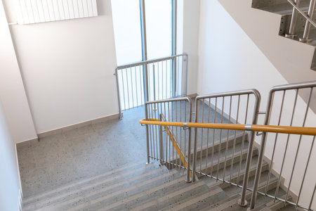 Indoor staircase with metal railing and wooden handrail. Bright modern design in public or...