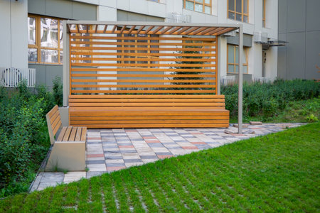 Wooden pergola with built-in bench in landscaped courtyard. Modern outdoor seating for residential...